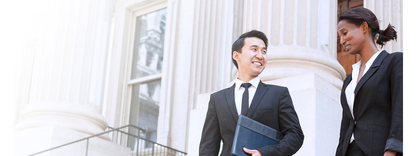 Two individuals in business attire standing in front of a modern office building, discussing work matters.